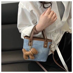 Bolso saco de mezclilla azul con ribete de cuero marrón y colgante de perrito en modelo