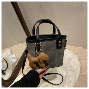 Detalle de bolso tote de lona con ribete de cuero negro y colgante de cachorro marrón
