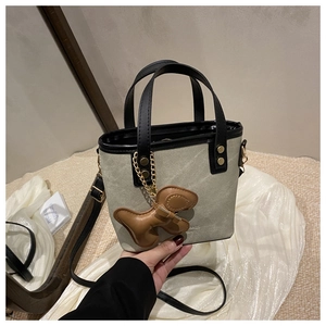 Detalle del bolso tipo cubo de tela con ribetes de cuero negro y colgante de perro