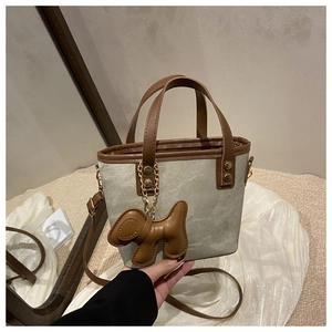 Detalle de bolso cubo de lona con ribete de cuero marrón y accesorio de perrito