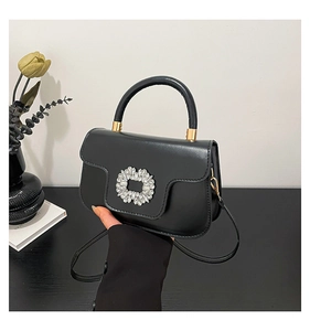 Detail of black crossbody bag featuring a sparkling rhinestone buckle and gold hardware
