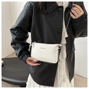 Close-up of a white leather crossbody bag with silver studs and golden Fashion lettering