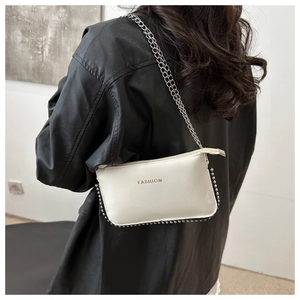 Detail of white PU crossbody bag featuring gold fashion lettering and silver beaded edges