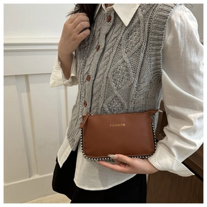 Detail of brown litchi leather crossbody bag with silver rivet studs and metal chain strap