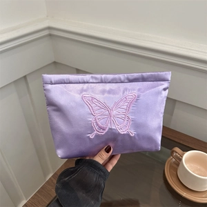 Elegant purple satin clutch bag with butterfly embroidery held in a casual indoor setting