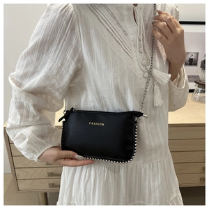 Detail of black crossbody bag with gold FASHION text and metallic beaded edge on white dress