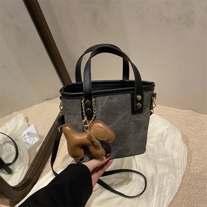 Bolso tipo cubo de lona gris con ribete de cuero negro y colgante de perro marrón