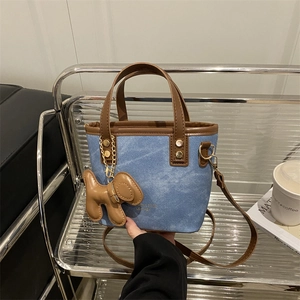 Bolso cubo de mezclilla azul con asas de cuero marrón y colgante de perrito