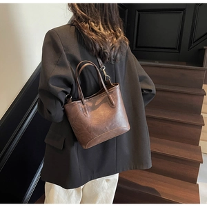 Detail view of a vintage brown leather bucket bag with top handle and crossbody strap