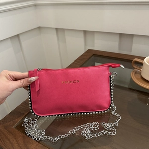 Magenta crossbody bag with silver beaded trim and chain strap on a glass table