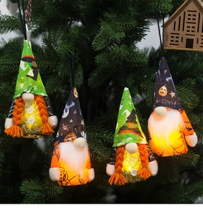Detail of four glowing Halloween gnome ornaments hanging on pine tree branches with LED light