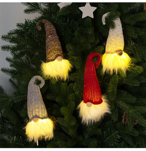 Macro shot of LED glowing Christmas gnomes hanging on a tree with warm yellow light