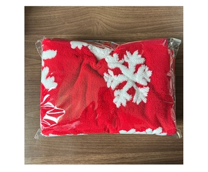 Detail of red plush Christmas tree skirt with white snowflake pattern in packaging