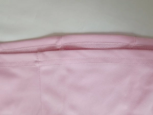 Dettaglio dell'abito rosa con cuciture a doppio ago e trama del tessuto a rete fine