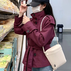 Short burgundy double-breasted trench coat with waist belt and cream cylinder bag