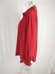 Side view of red chiffon shirt featuring smocked cuffs and back neck tie detail