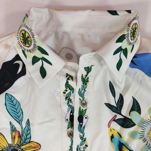 Détail du col d'une chemise blanche en satin avec motifs floraux et serpent vibrants