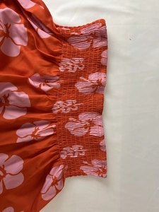 Detail of tropical floral print fabric with elastic smocking waist and vibrant orange patterns
