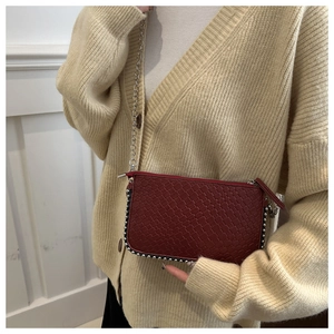 Close-up of burgundy woven clutch bag with silver chain strap and beaded trim detail