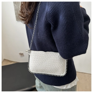 Close-up of white woven square bag with decorative metal beads and silver chain strap