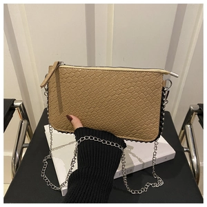 Detail of khaki crocodile pattern crossbody bag with silver chain strap and metal rivets