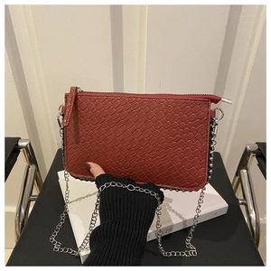 Detail of red crocodile texture envelope bag with silver chain and metal stud trim