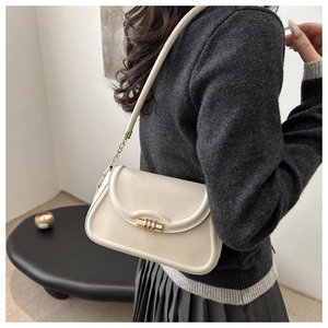 Detail of cream shoulder bag with golden buckle and chain strap shown on a model