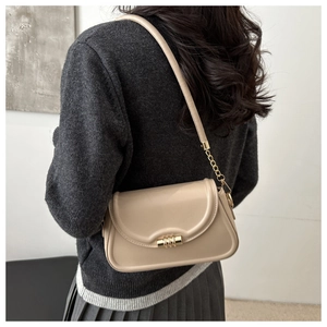 Detail of beige leather shoulder bag with gold cylinder lock and chain strap on model