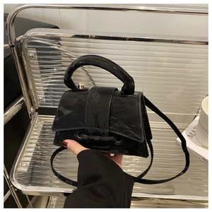 Detail of black pleated mini handbag with round handle and gold hardware in a modern setting