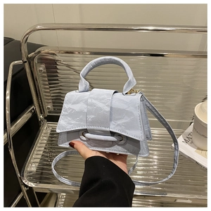 Detailed view of light blue wrinkled faux leather mini handbag on a textured glass shelf