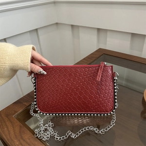 Red woven clutch bag with silver bead trim and chain strap on a wooden table