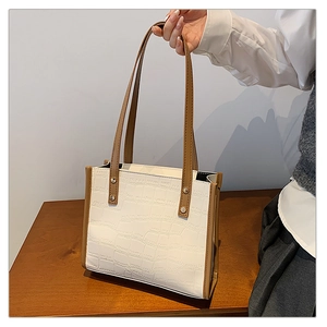 Close-up of white crocodile pattern tote bag with brown contrast trim and silver rivets