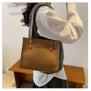 Detail of a brown crocodile texture tote bag with gold studs and shoulder straps