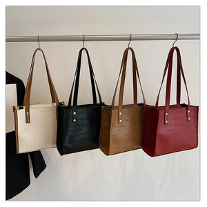 Detail view of crocodile-patterned tote bags in four colors with gold metal rivets