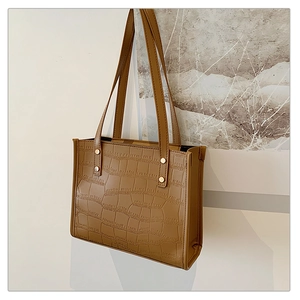 Detail view of brown crocodile embossed tote bag with gold rivets and leather texture