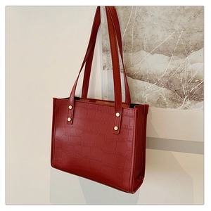 Detail of red crocodile pattern tote bag featuring gold stud accents and slim straps
