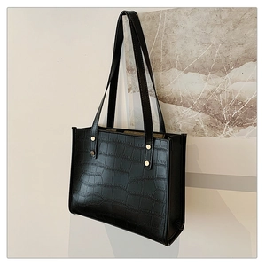 Close-up of black crocodile pattern tote bag with gold rivet accents on the handle