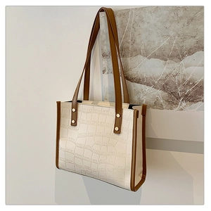 Detail view of cream tote bag with brown trim, crocodile pattern and gold rivet accents