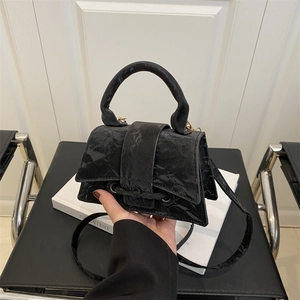 Chic black crinkled leather trapezoid handbag with top handle and crossbody strap