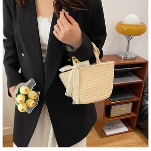 Detail of hand-woven beige straw tote bag featuring a delicate white lace ribbon bow