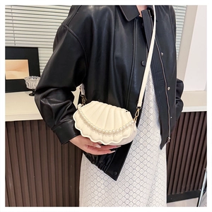 Close-up of shell-shaped white shoulder bag with pearl chain detail worn by a model