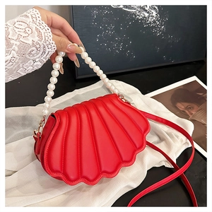 Detail of red shell-shaped crossbody bag with pearl handle and golden hardware