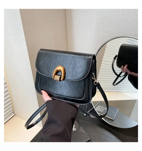 Detail of a black square crossbody bag featuring a distinctive gold U-shaped metal buckle