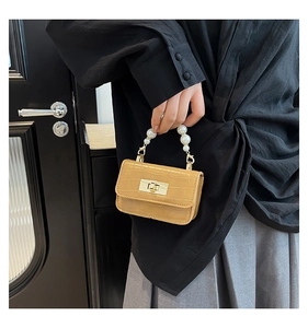 Détail du sac effet croco avec poignée en perles et fermoir rotatif doré élégant