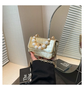 Macro detail of gold crocodile-embossed mini bag with pearl handle and metal lock