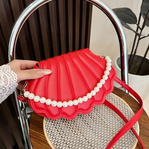 Elegant red shell-shaped crossbody bag with pearl chain on a stylish wooden chair