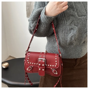 Detail of red vintage leather shoulder bag with silver rivets and metal eyelets on model