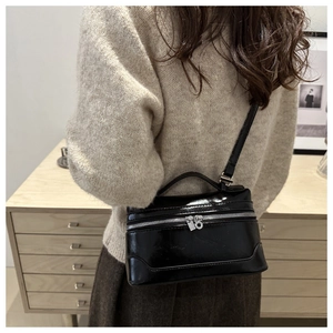 Détail d'un sac boîte noir brillant avec fermetures éclair argentées porté par un mannequin