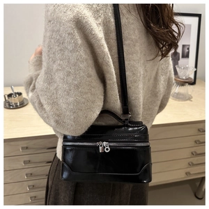 Détail d'un sac boîte noir brillant avec fermetures éclair argentées et poignée