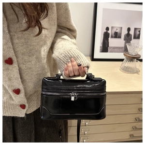 Gros plan d'un sac boîte rétro noir brillant tenu par un mannequin pour un look mode